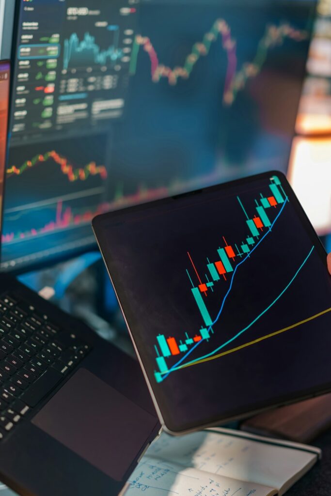 Mano sujetando una tablet con un gráfico financiero sobre un portátil.